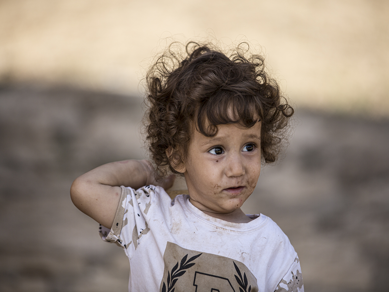 Ce garçon l'air à la fois songeur et malicieux. Il tient une pierre dans sa main droite, posée derrière sa tête, ajoutant une touche d'espièglerie à l'instant.